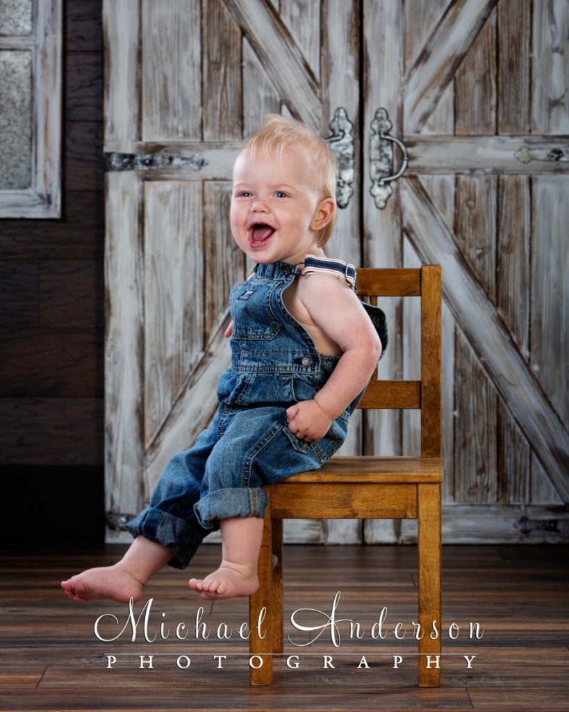 A cute one-year-old boy sitting a wooden chair.