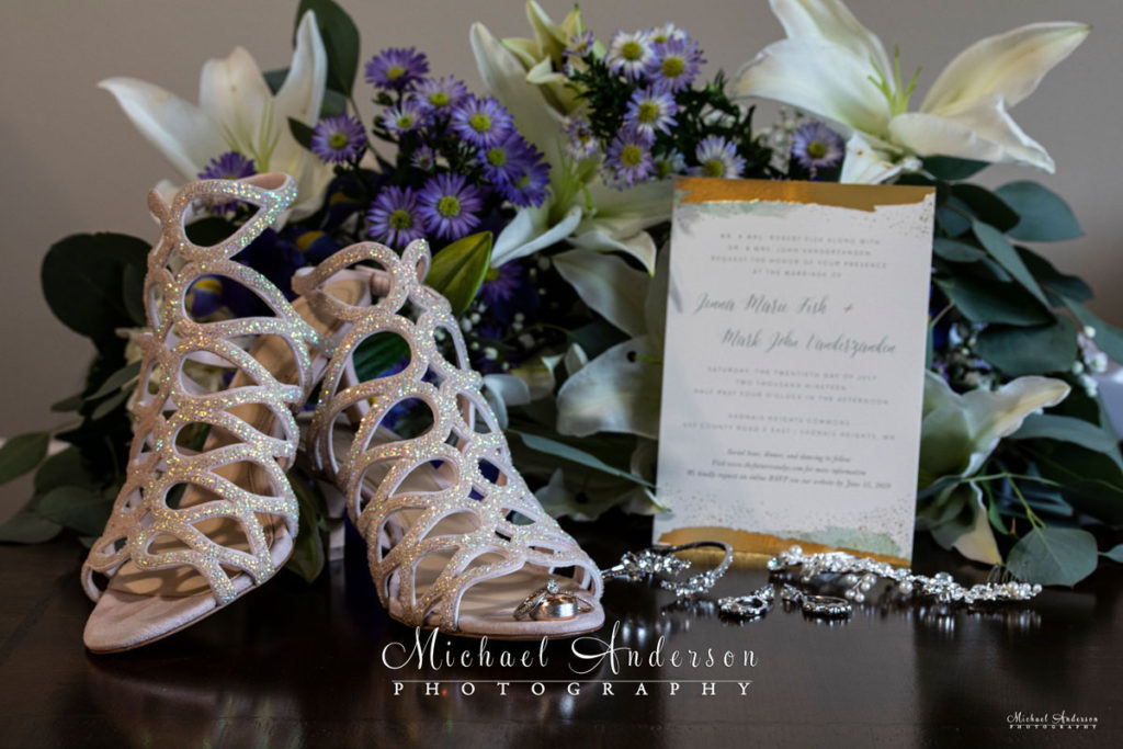 Wedding photo of the brides shoes, jewelry, wedding rings, flowers, and invitation.