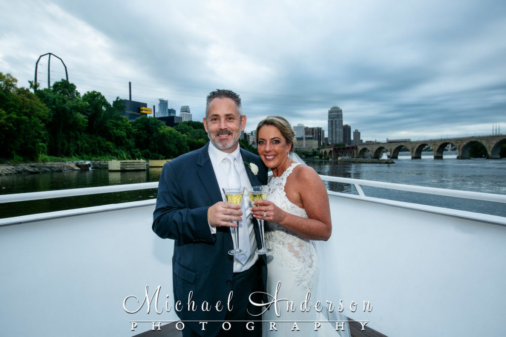 The bride and groom enjoy champagne onboard the Paradise Lady with downtown Minneapolis behind them.