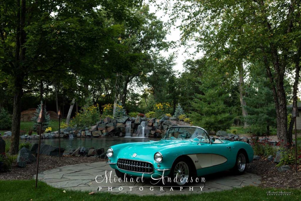 Daylight photo of a mint condition 1957 C1 Corvette Convertible with a waterfall in the background.