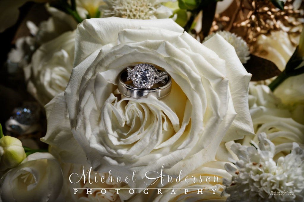 A cool light painted wedding photo of the bride and groom's wedding rings in a white rose.