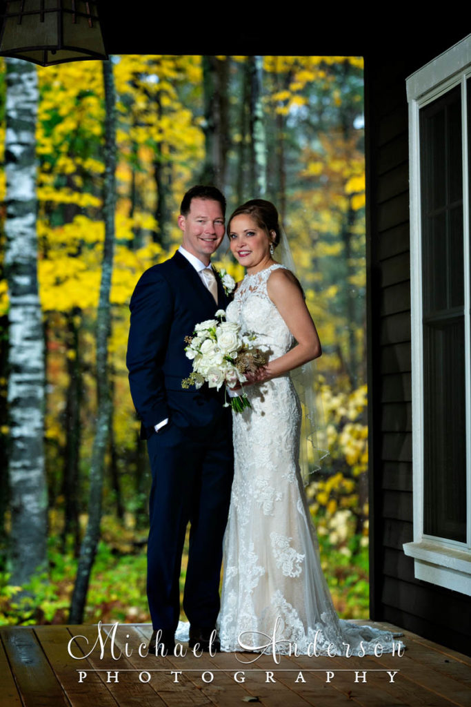 The bride and groom take cover from the snow under a porch roof during their Grandview Lodge wedding day.