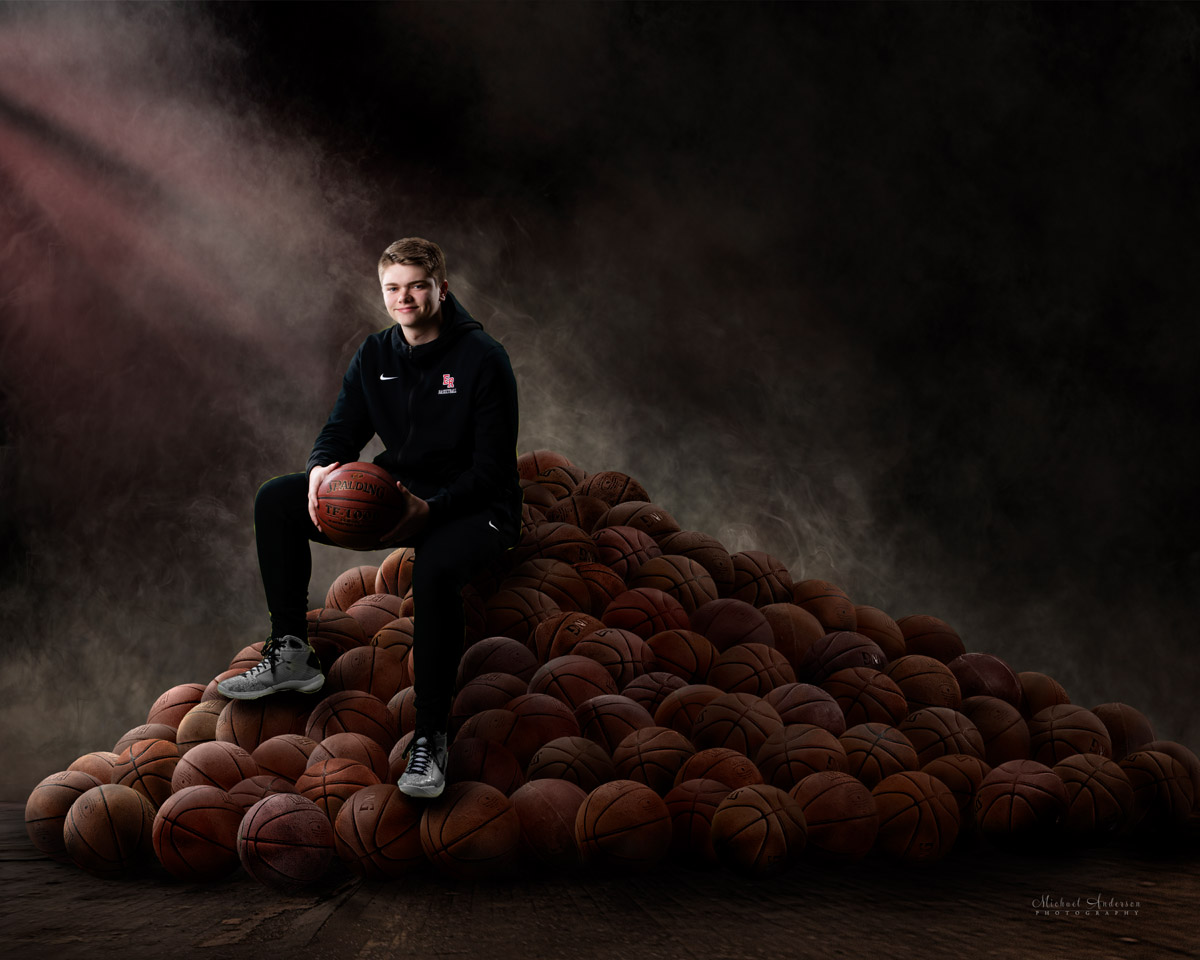 Elk River High School senior portrait green screen composite. A basketball player sitting on a pile of basketballs.