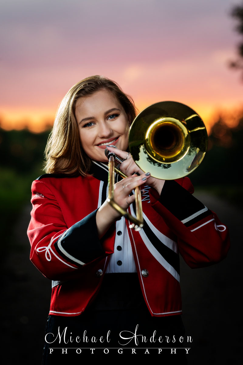A Centennial High School Marching Band senior girl, in uniform, and holding her trombone. Photo taken at sunset at Long Lake Park in New Brighton, MN.