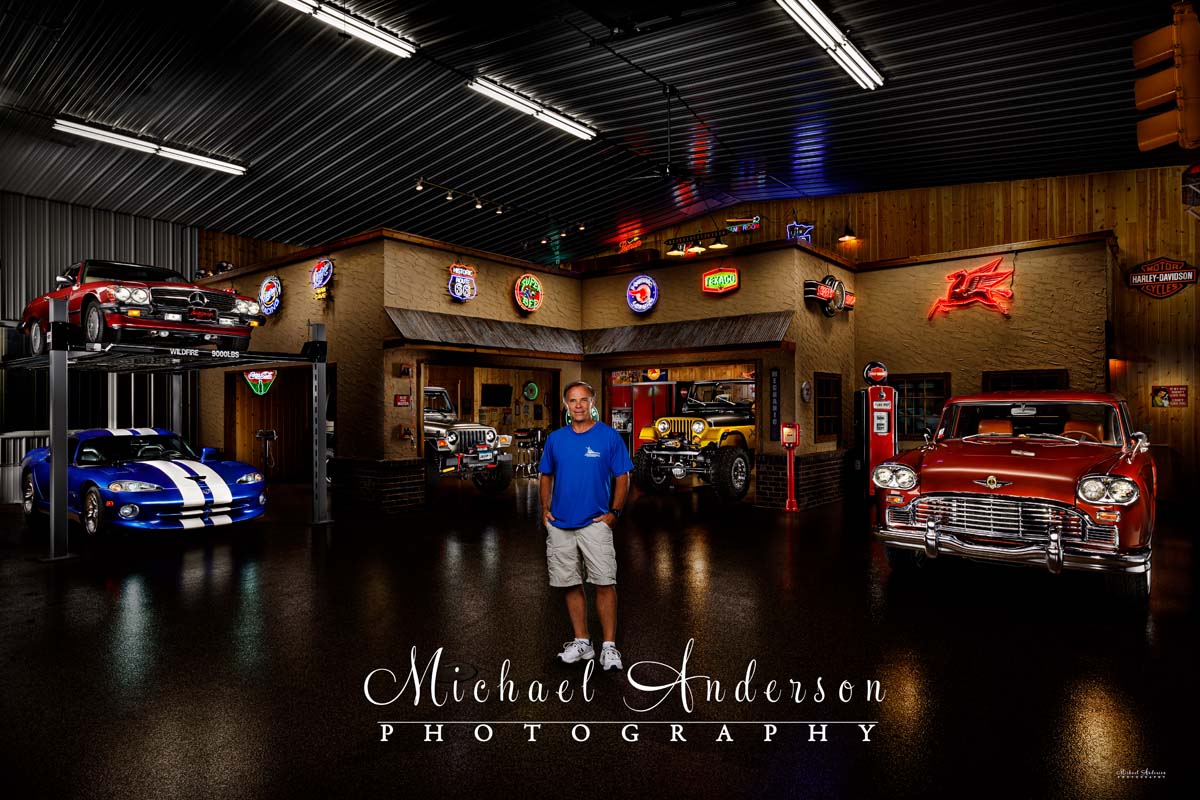 A stunning light painted photograph of a vintage garage inside of a Garage Condo! A total of five vehicles are in the photo too! The owner is in the photograph as well.