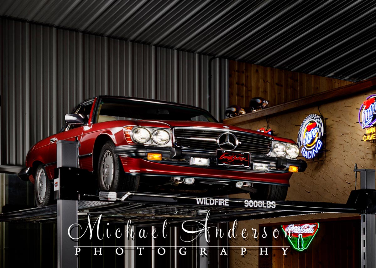 A light painted photograph of a 1989 Mercedes 450SL, on a Wildfire Lift, in a Man Cave.