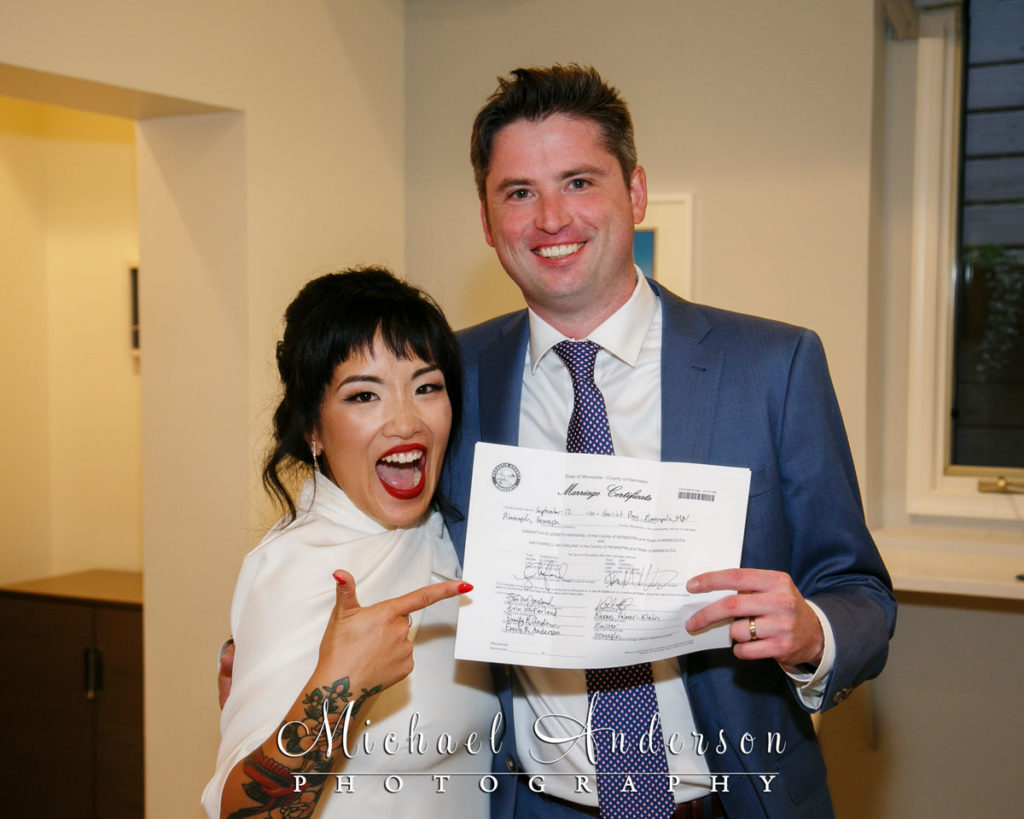 A fun wedding photograph of the newlyweds holding their marriage certificate.