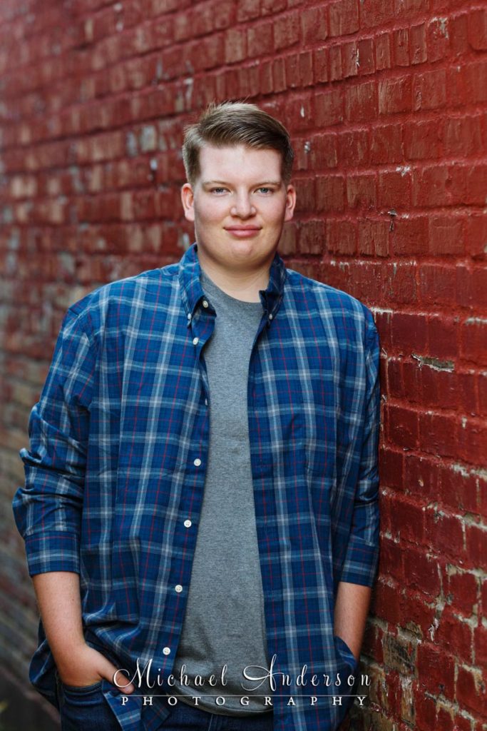 A nice senior photo of a boy leaning on a red brick wall.