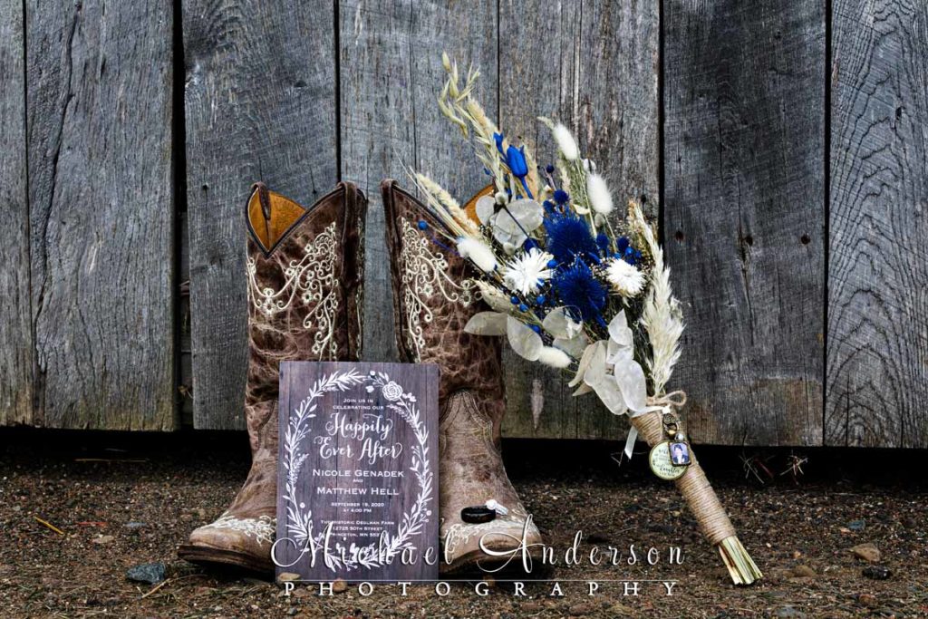 Wedding detail photo of the brides cowboy boots, wedding rings, her bouquet, and the wedding invitation.