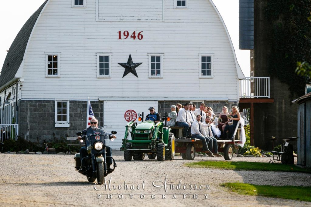 A fun wedding photo of the wedding party on a hay wagon being laid by the wedding officiant on a Harley.