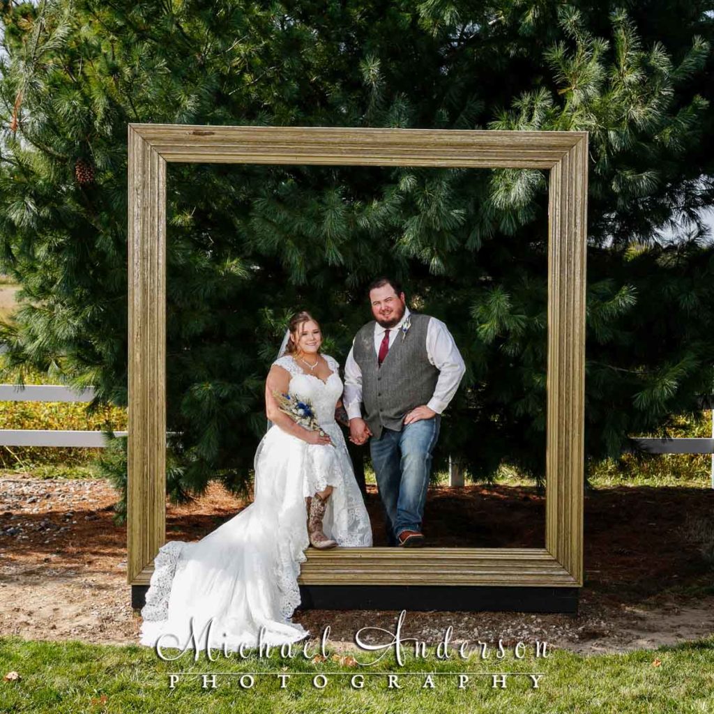 Bride and groom stand=ing a a huge square frame at Deglman Farm.