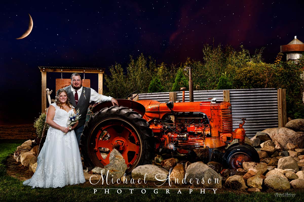 A cool light painted wedding photo of the bride and groom, a farm tractor, under a waxing crescent moon.