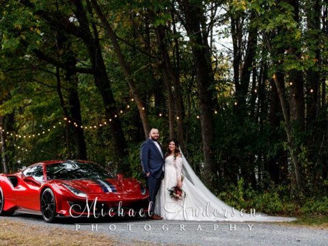 Th bride and groom by a red Ferrari at their wedding reception.