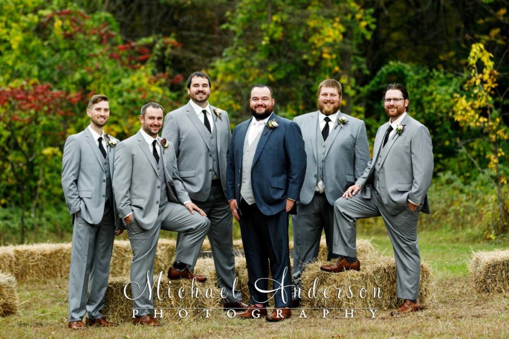 The groom and his groomsmen by some hay bales.