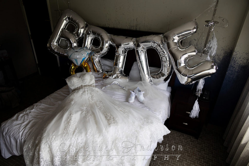 The bride's pretty dress, veil, and shoes, and jewelry lying on a hotel bed.