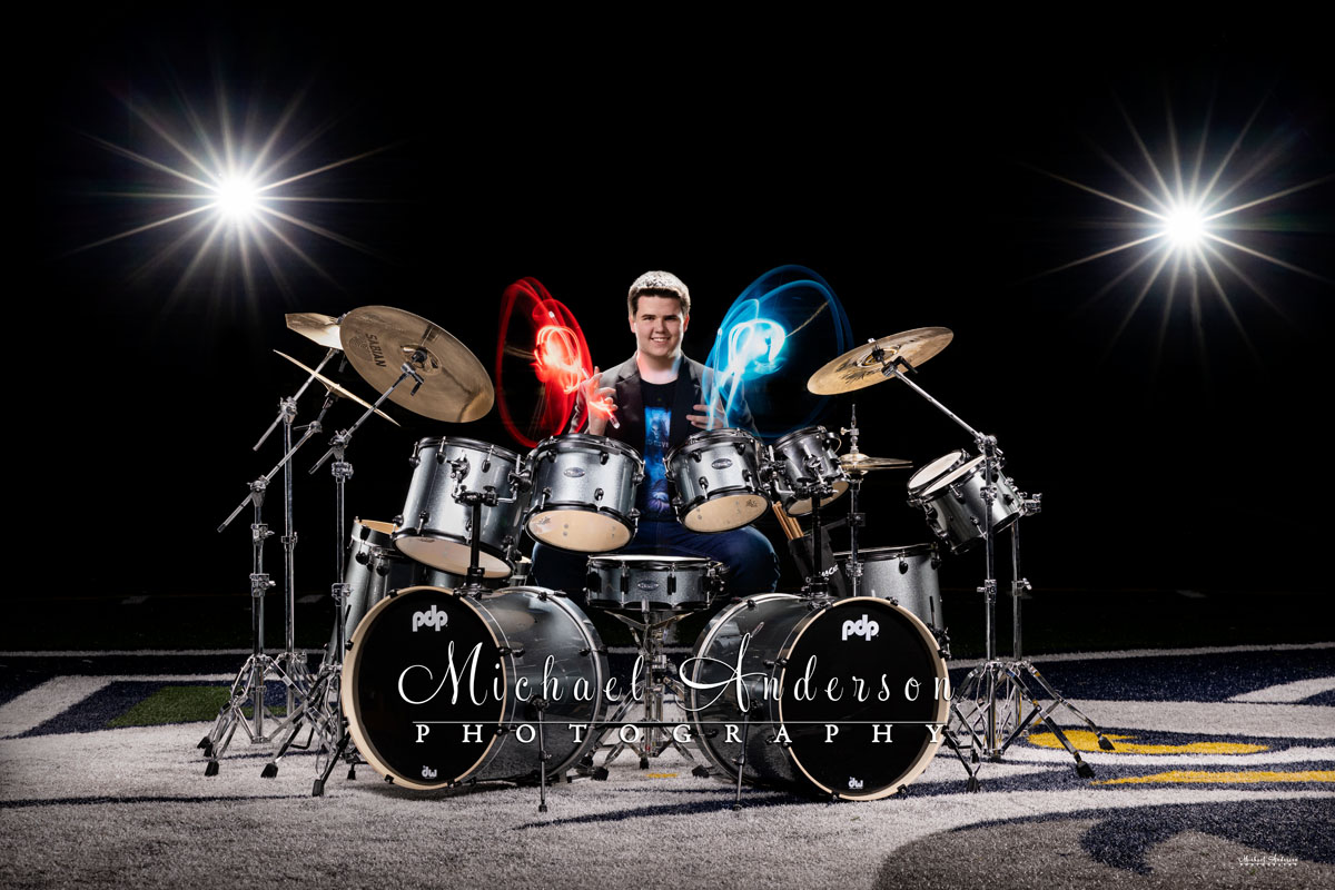 A cool light painted senior photo of a boy and his drum set, holding lighted drum sticks, on the football field at Totino Grace High School in Fridley, MN.