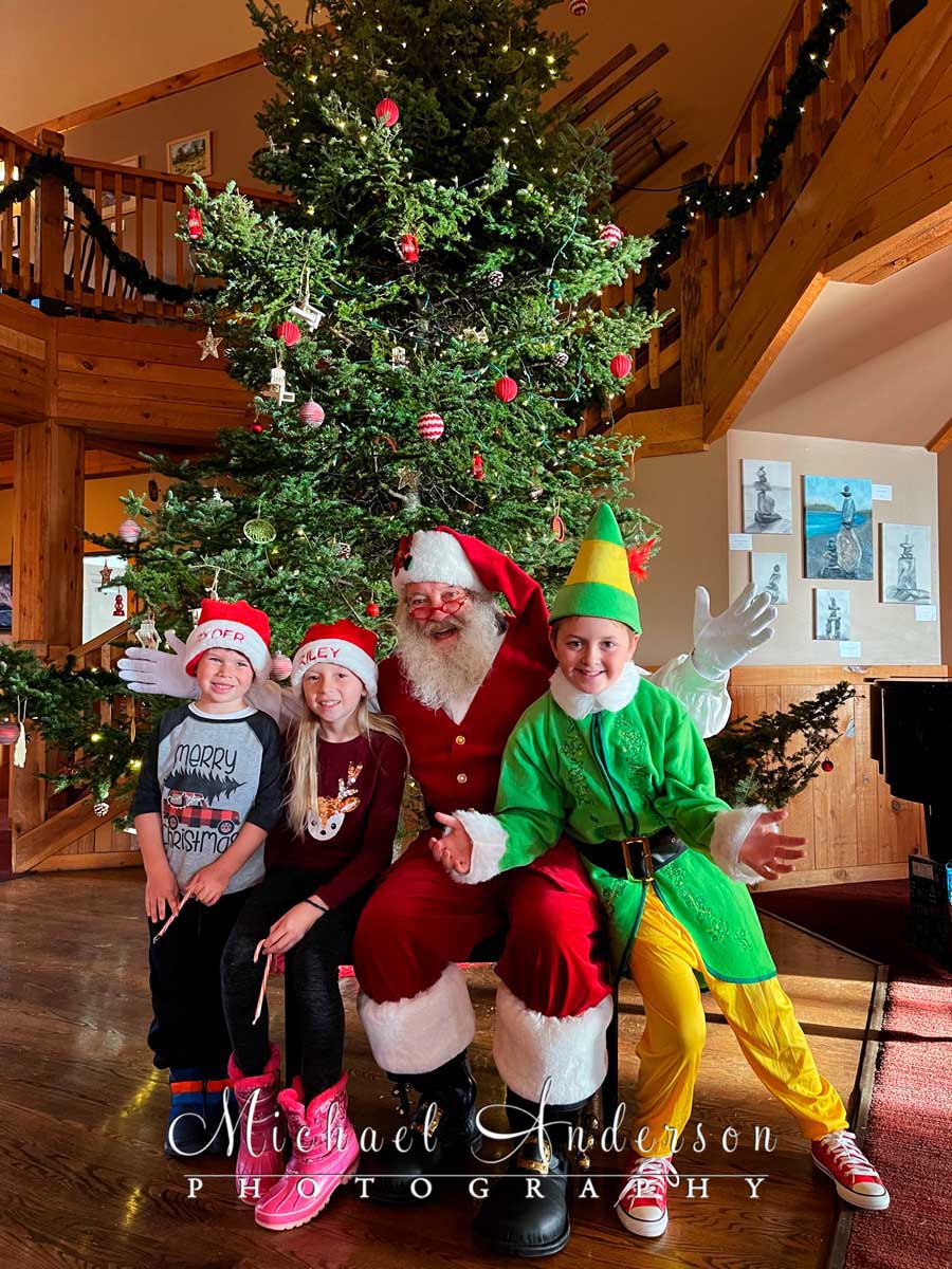 A photo of Santa, one of his elves, and two kids in front of the Christmas Tree at Cove Point Lodge, Lake Superior, MN.