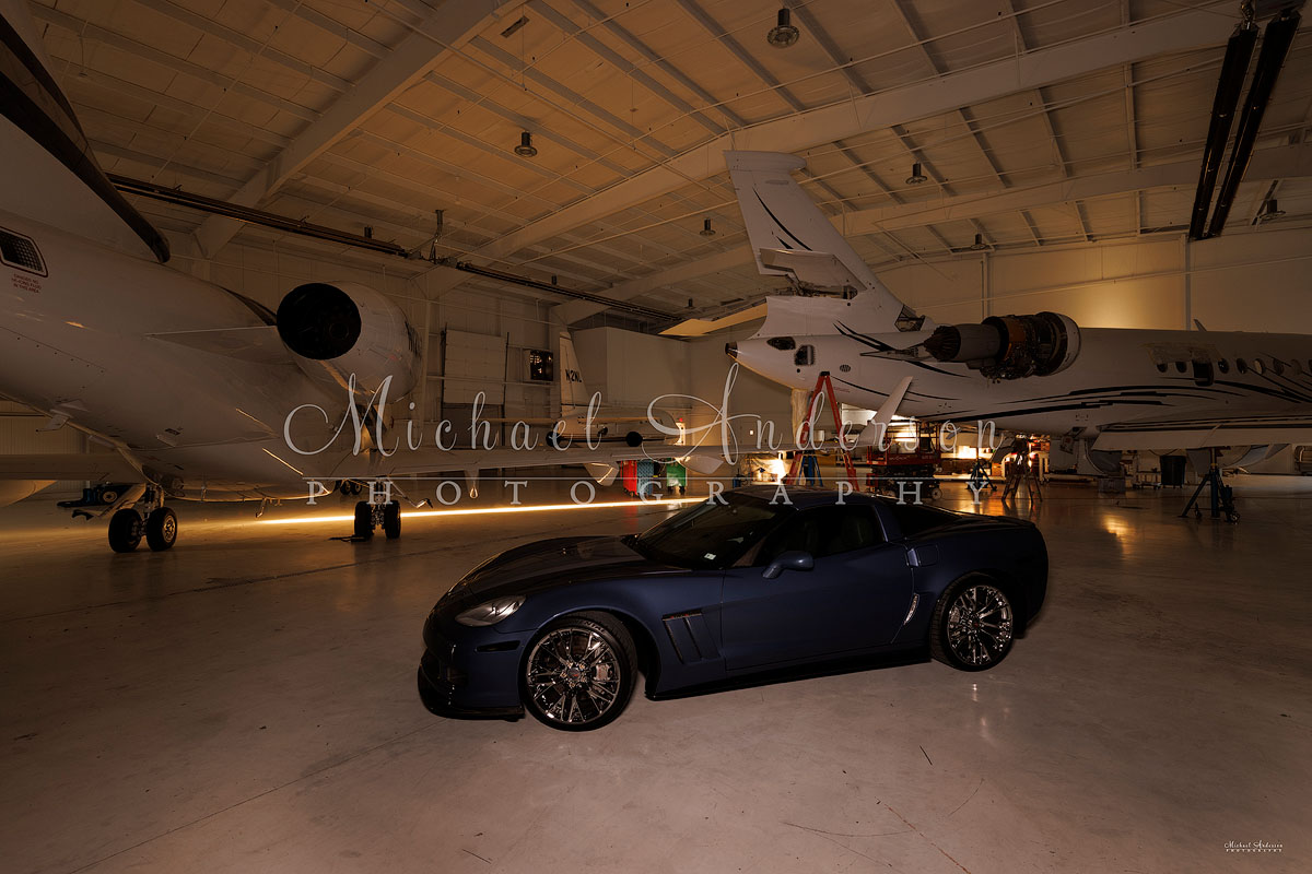 Photograph of a 60th anniversary Corvette Grand Sport and 3 corporate jets in a hanger.