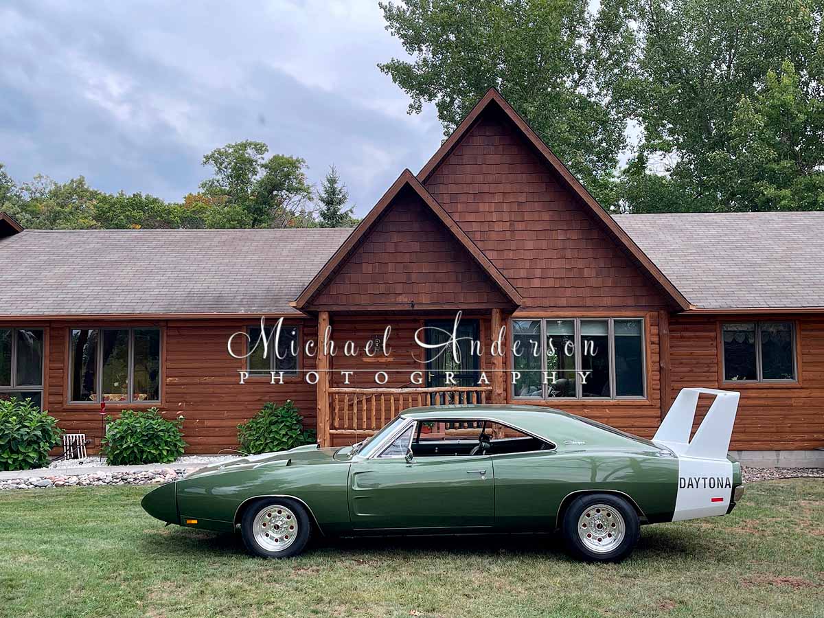 A rare 1969 Dodge Daytona in front of a log home.