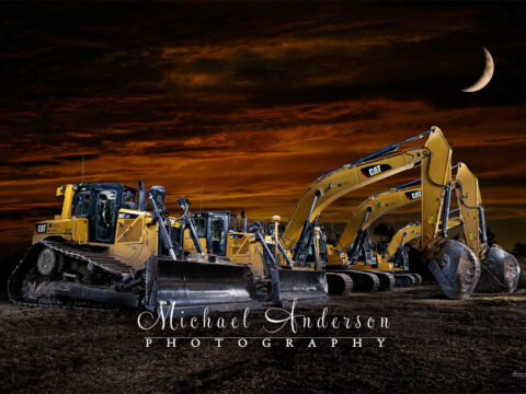 A cool light painted photograph of five heavy construction vehicles and a stunning sunset.