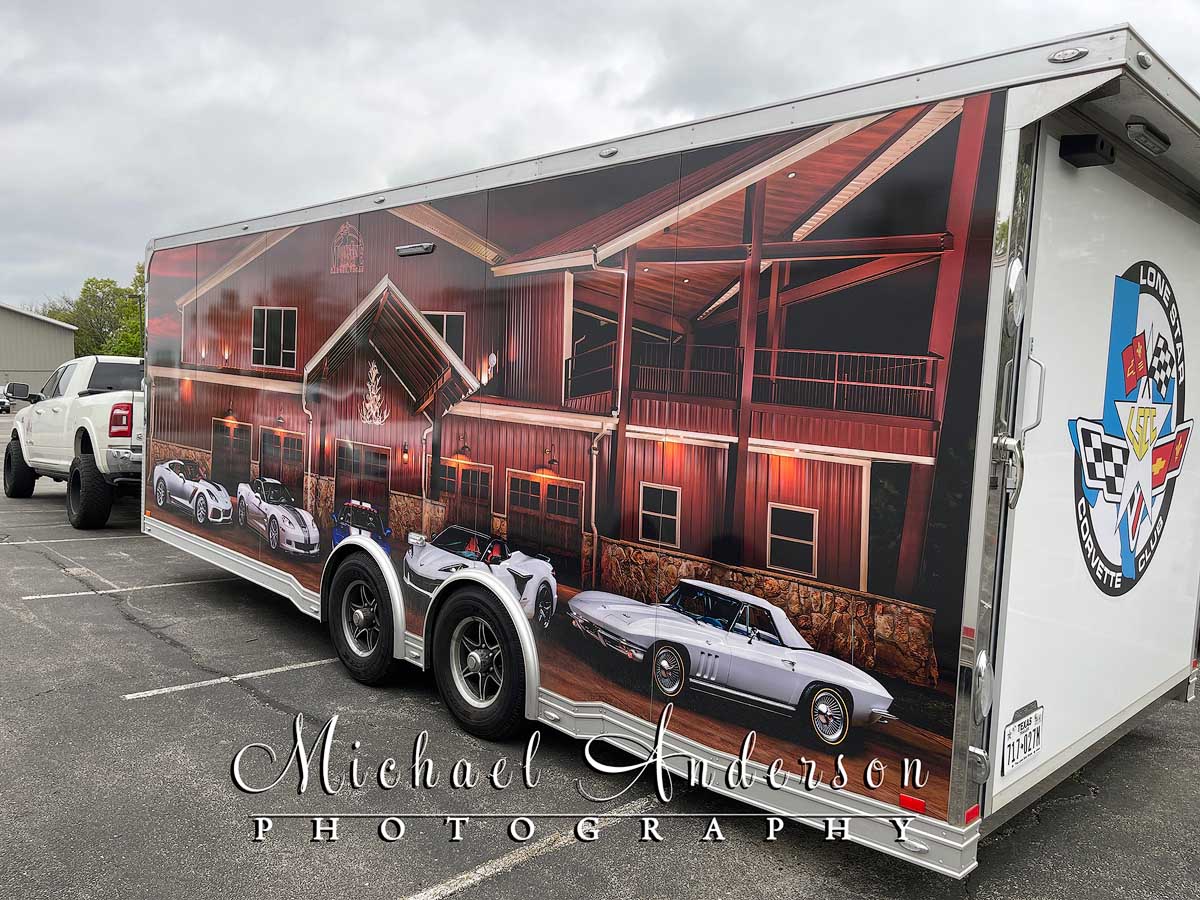 A car transport trailer with a light painting of five Corvettes wrapped on it.