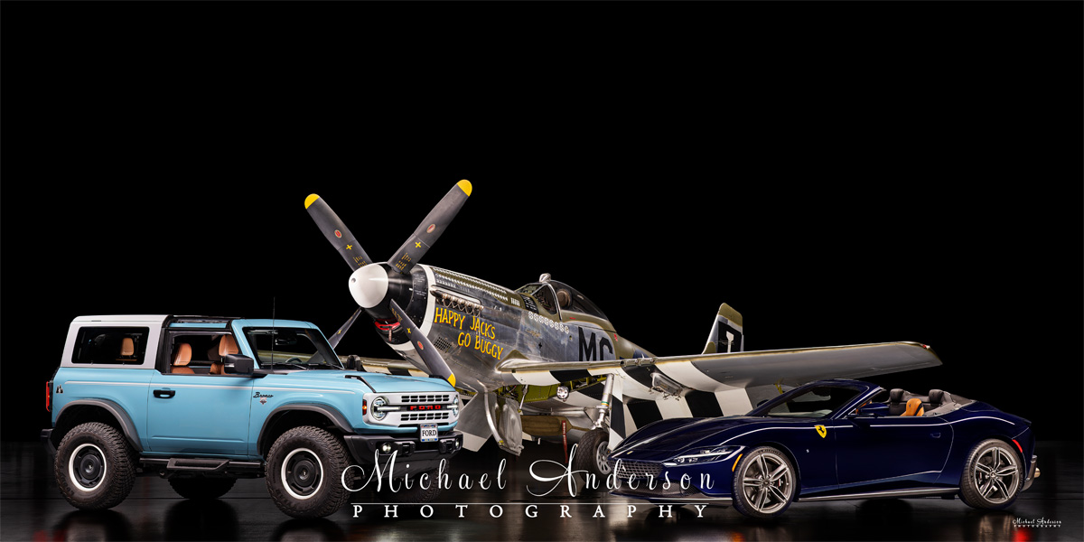 A really cool light-painted photograph of three amazing vehicles. From left to right is a 2024 Ford Bronco Heritage Edition, the famous P-51 D Mustang “Happy Jack's Go Buggy”, and a 2025 Ferrari Roma Spider!
