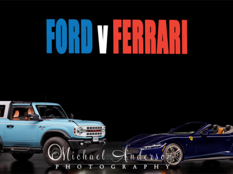 A really cool light-painted photograph of a Ford vs Ferrari. The Ford is a 2024 Ford Bronco Heritage Edition. The Ferrari is a blue 2025 Ferrari Roma Spider.